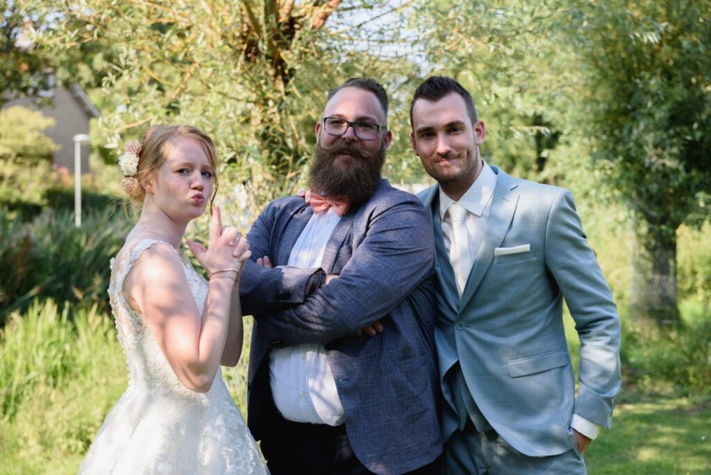 Bruidspaar poseert lachend met trouwambtenaar Jorg in de tuin