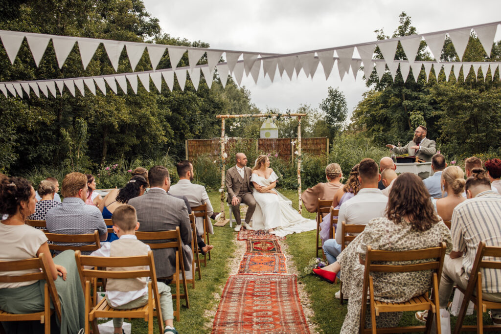 Buitenceremonie met gasten, het bruidspaar onder de bloemenboog